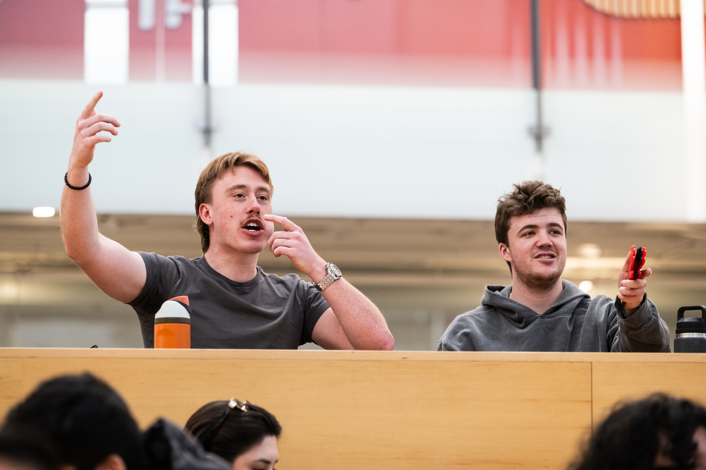 Two students sit side by side cheering and pointing as they watch the women's hockey team play.