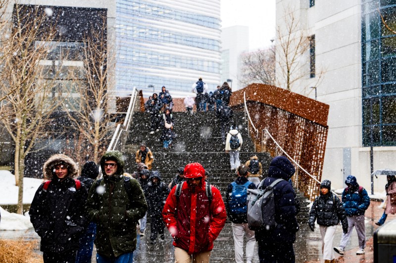 Students walks on a bridge between buildings as snow falls.
