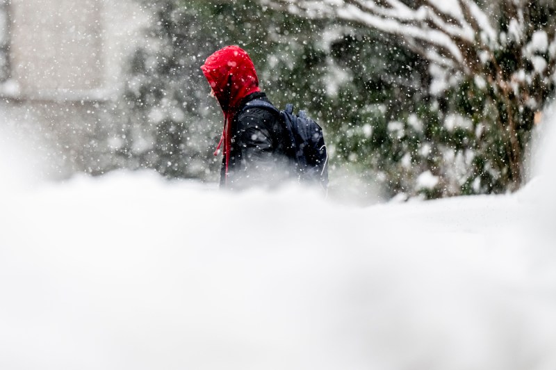 A person dressed in black and red walks through snow.