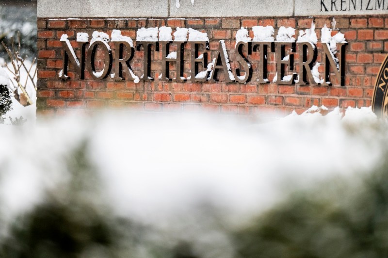A Northeastern University sign on brick is covered in snow.
