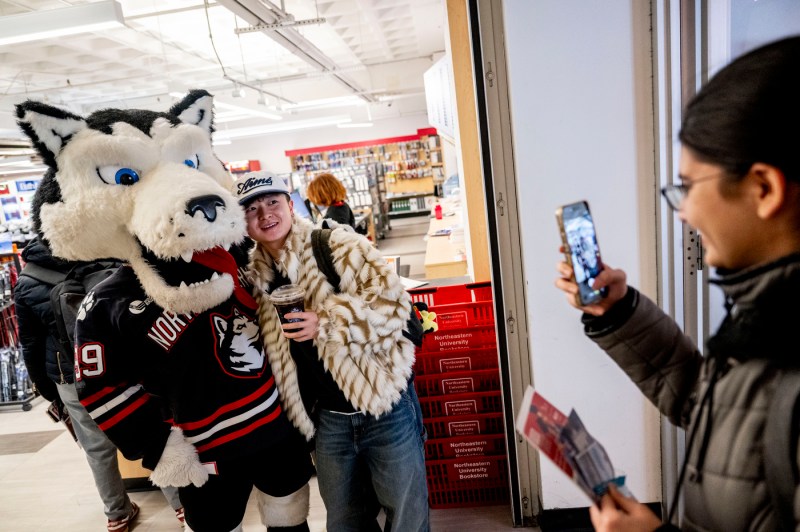 A person holding a cell phone takes a photo of Paws the mascot posing with an individual.