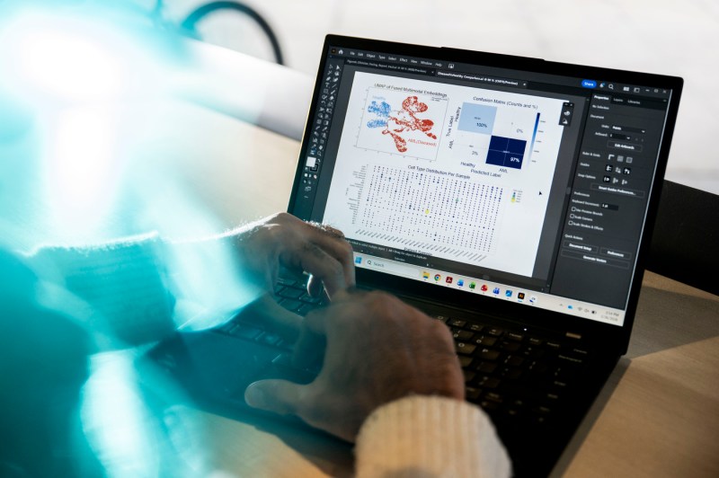 A close up of two hands typing on a laptop illuminated by a bright blue flare of light.