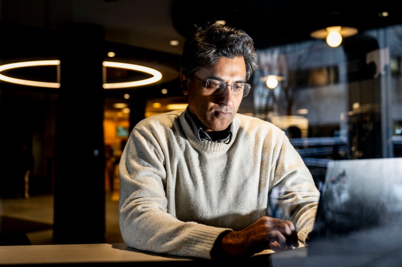 Inside a darkly lit room, a close up of a person in a sweater typing on a laptop. 