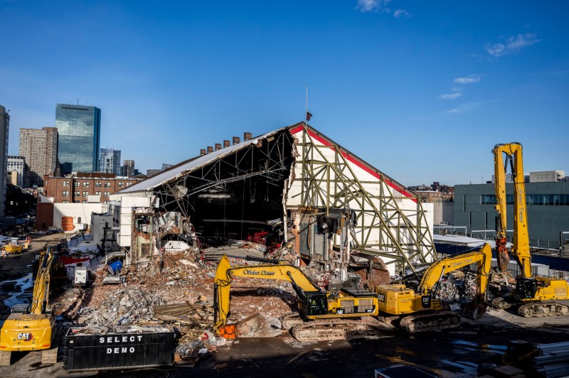A wide shot of an active construction site where heavy machinery brings down the former Matthews Arena, with debris and rubble visible throughout the surrounding area.