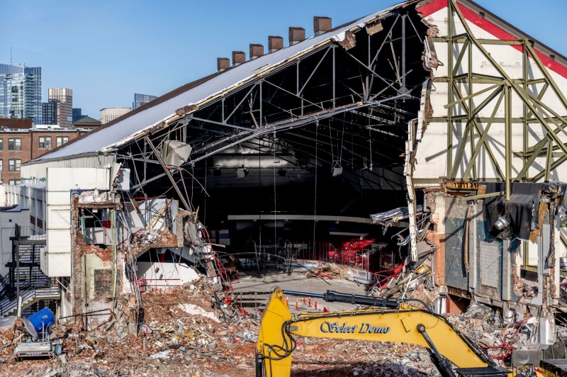 An active construction site where heavy machinery brings down the former Matthews Arena, with debris and rubble visible throughout the surrounding area.