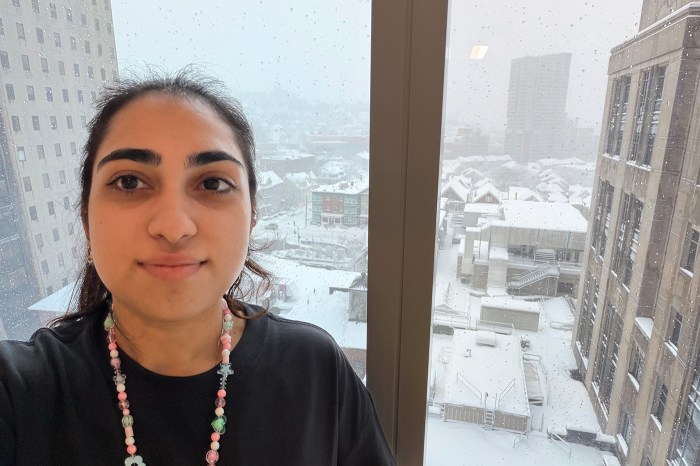 A co-op takes a selfie with a snowy urban view seen out the window in the background.