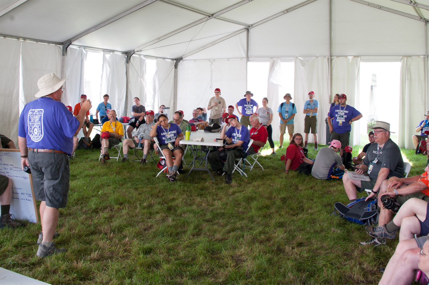 A National Jamboree staff member speaks to other volunteers and staff in a big white tent.