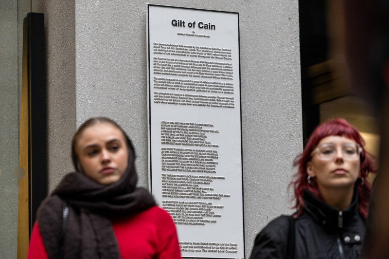 People watch a speaker with a plaque behind them