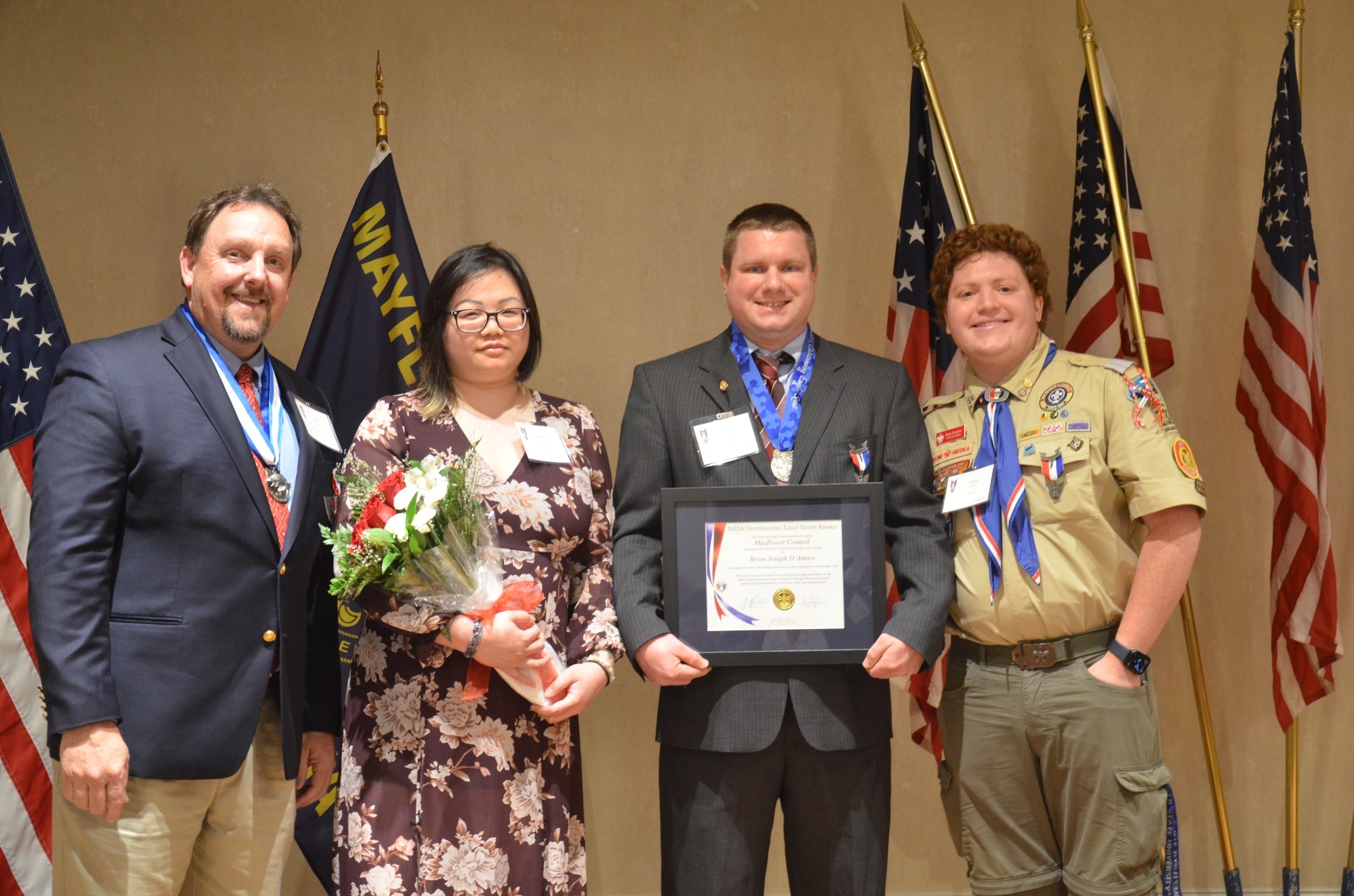 A group of four people pose for a photo with their awards with American flags and a Mayflower Council flag behind them.