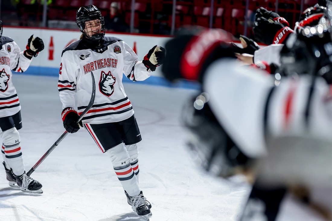 Alessia Baechler wearing a Northeastern hockey jersey and gear skating down a line of her teammates giving them fist bumps.