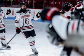 Alessia Baechler wearing a Northeastern hockey jersey and gear skating down a line of her teammates giving them fist bumps.