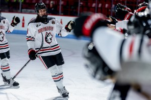 Alessia Baechler wearing a Northeastern hockey jersey and gear skating down a line of her teammates giving them fist bumps.
