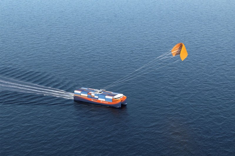 A cargo ship moving through open water as a large orange kite pulls it forward using wind power.