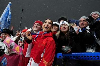 Eileen Gu poses in front of a group of fans at the Olympics with a medal around her neck.