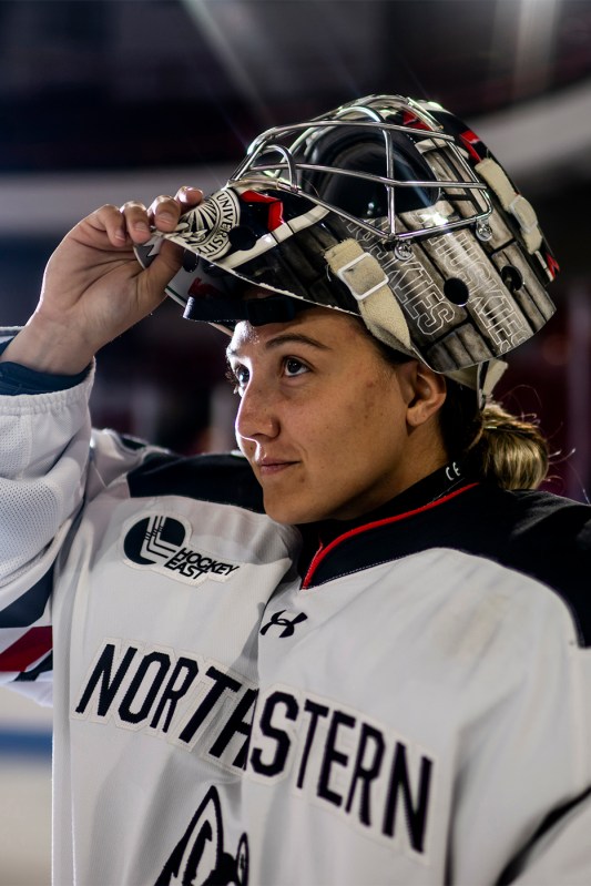 Gwyneth Philips takes off her goalie's helmet while looking toward a light off in the distance.