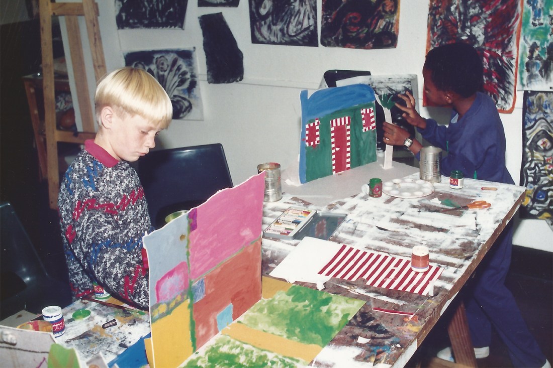 Two young students paint at a cluttered work table inside the Johannesburg Art Foundation building. 