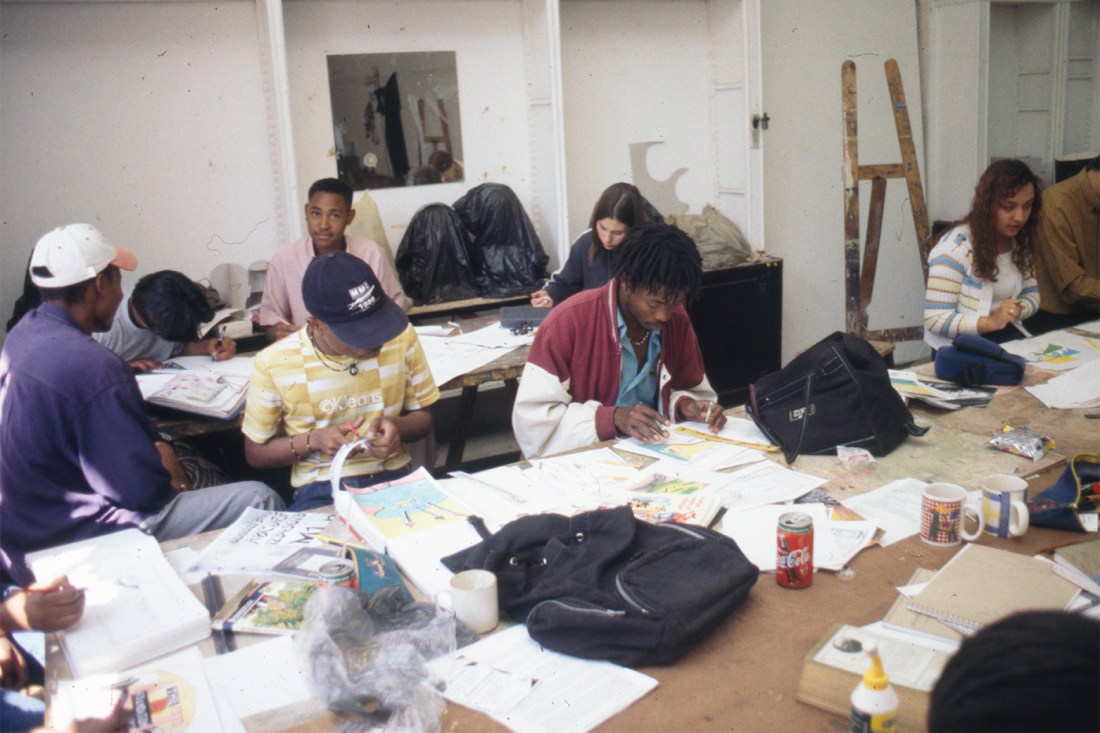 Students sitting at two tables covered in art materials, backpacks, cans of soda and mugs, during a class at the Johannesburg Art Foundation.