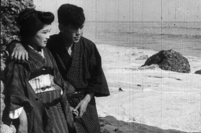A Japanese woman and man stand together on a beach in a black and white still image from "The Oath of the Sword."