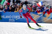 Johannes Hoesflot Klaebo wearing a blue and red ski suit cross country skis across the snow in front of a crowd at the 2026 Winter Olympics.