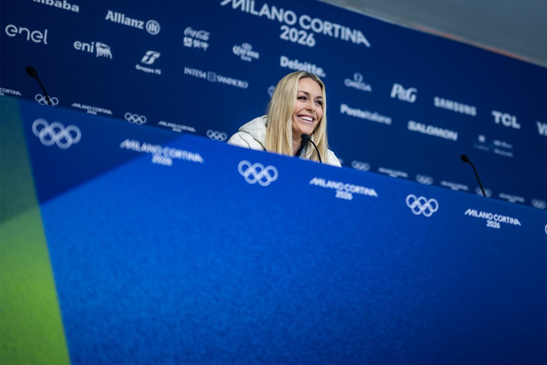 Lindsey Vonn sitting at a press conference with Olympics branding on the backdrop and table she is sitting at.