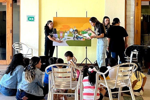 Two participants engage in one-on-one conversation at a table with laptops and materials in a bright classroom setting.
