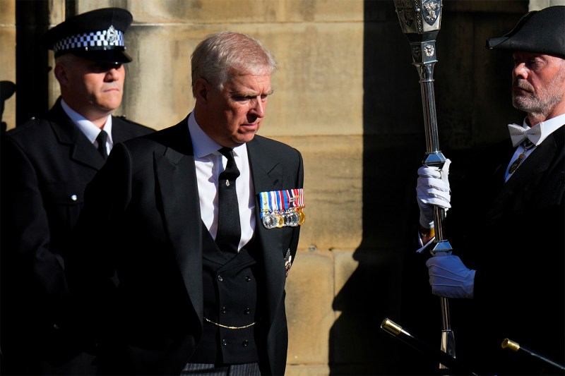 Former Prince Andrew in a black suit stands next to two men, also dressed in suit and tie.