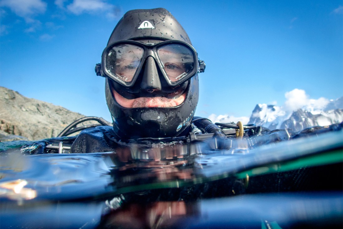 A diver at the water's surface wearing a mask and hood, partially submerged.
