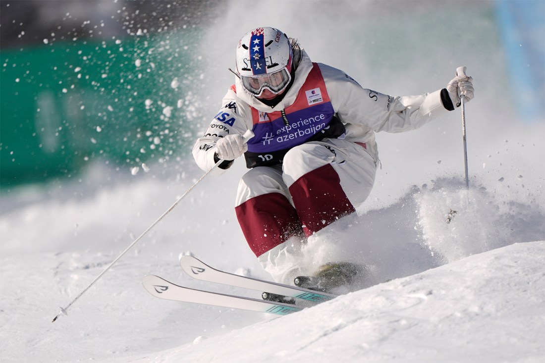 A U.S. skier plunges down a snowfield, knees bent and together, wearing thick snow clothing.