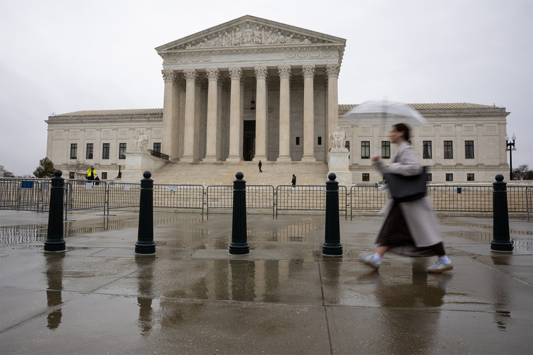 The exterior of the U.S. Supreme Court building on a rainy day. A person walks by carrying an umbrella.