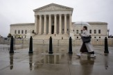 The exterior of the U.S. Supreme Court building on a rainy day. A person walks by carrying an umbrella.
