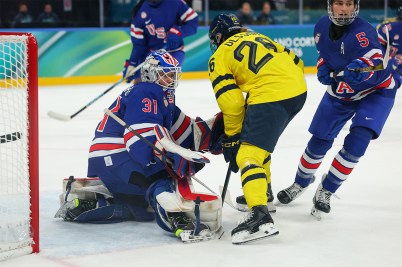 An ice hockey player in a yellow jersey faces the goaltender of Team USA at the 2026 Winter Games.