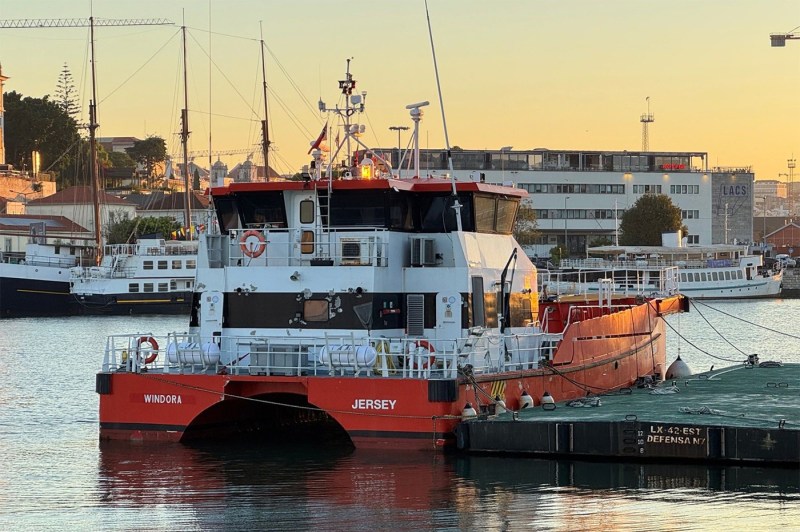 A small red and white vessel docked at a harbor, with equipment and ropes visible on deck at sunset. 