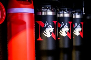 A line of black water bottles with the red Northeastern N and the Husky logo.