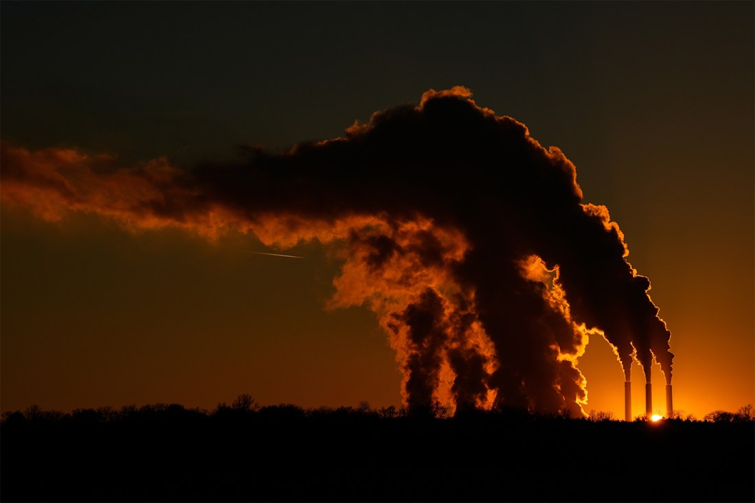 Smoke stacks, set against a sunset, send plumes of gas into the air.