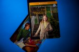 Two American Girl books displayed on a blue surface, with 'The Tangled Web: A Julie Mystery' prominently featured showing a young girl in a patterned cardigan standing on stairs, and another book partially visible underneath showing a figure with red hair in green clothing.