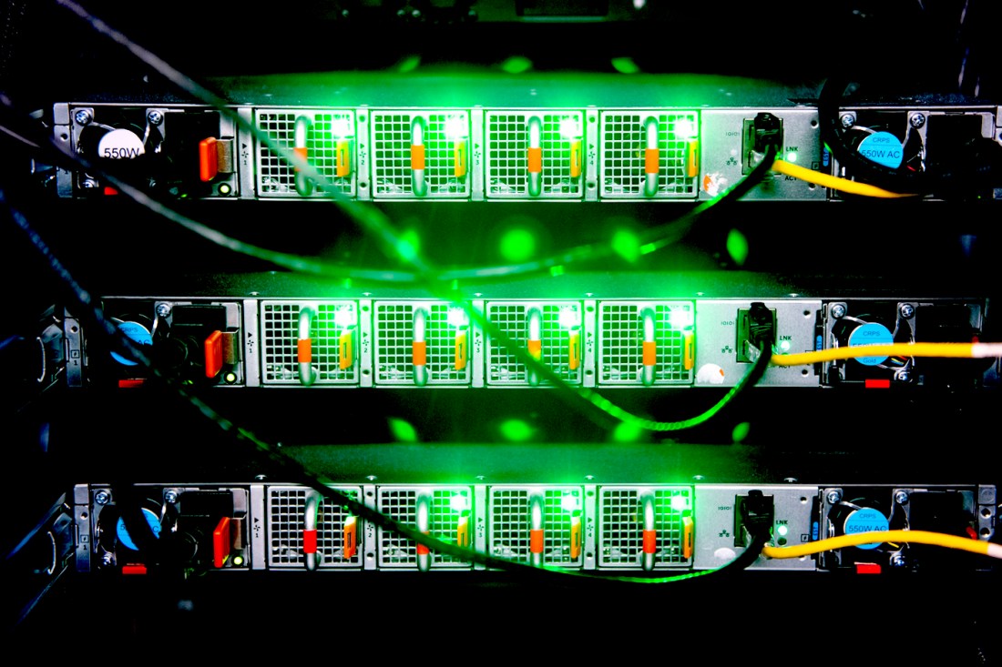 Close-up of stacked network servers with rows of ports glowing green and multiple ethernet cables connected, viewed from the front.