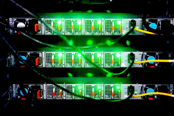 Close-up of stacked network servers with rows of ports glowing green and multiple ethernet cables connected, viewed from the front.