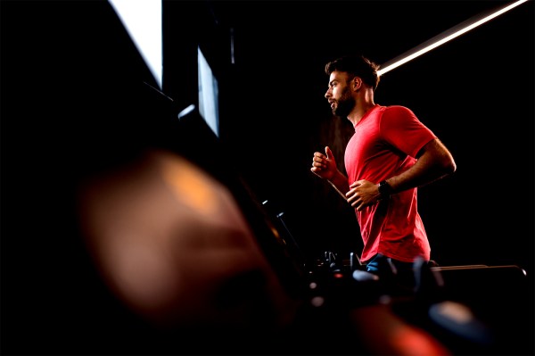 A man wearing a red shirt is running on a treadmill indoors.