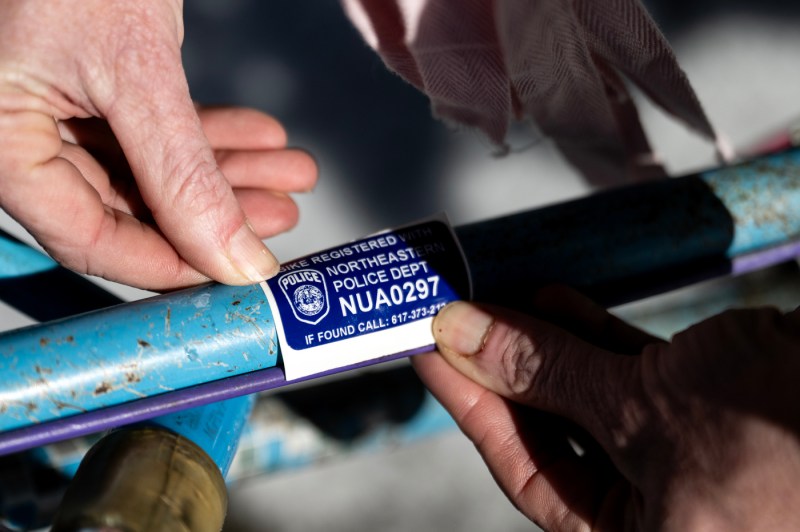 A closeup image of hands putting a blue bike registration sticker on a bike frame.