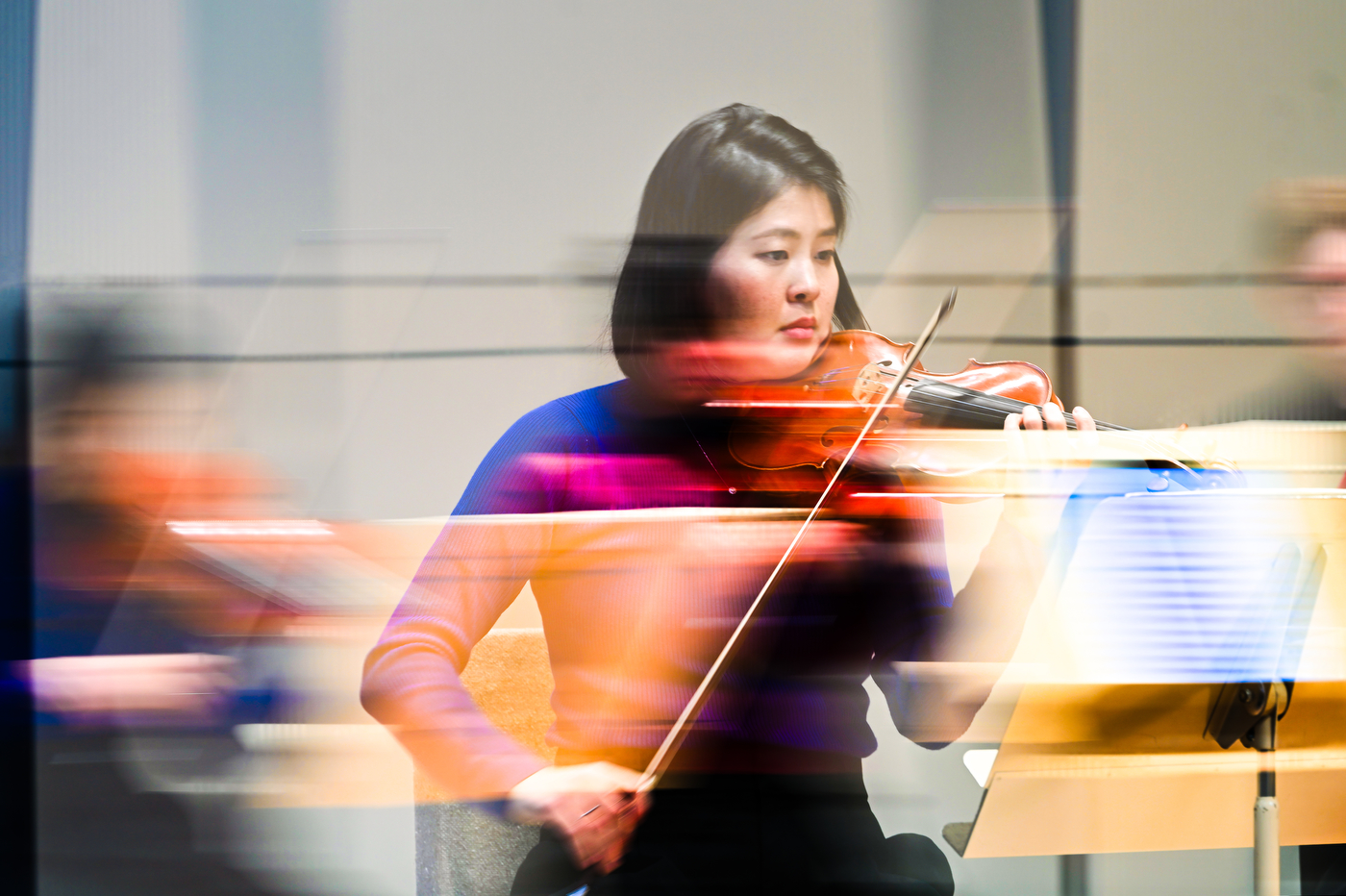 A woman in blue shirt plays the violin, motion is depicted with bluring lines.