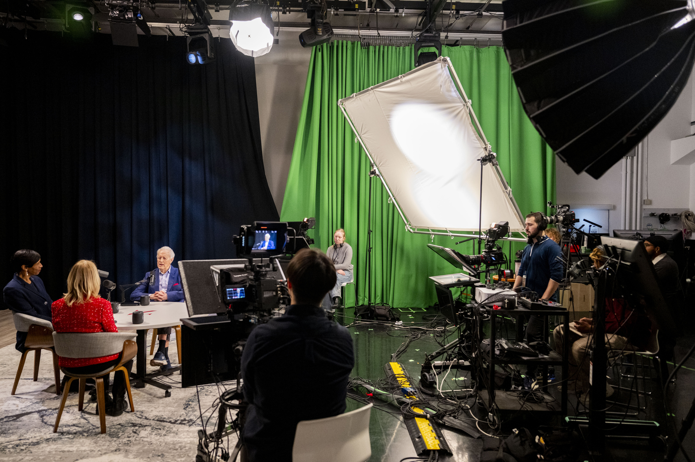 A film crew surrounds Sheila Puffer and Daniel McCarthy during taping in the NGN studio at Northeastern University, with a green screen visible in the background.