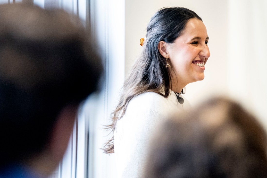 Melina Coy wearing a white shirt and a lapel microphone smiling.