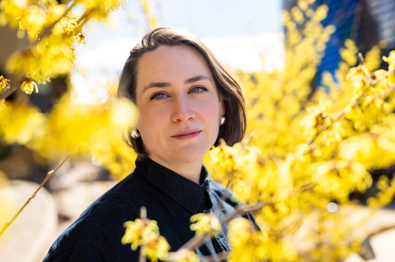 A professor poses for a portrait surrounded by yellow flowers and sunlight.