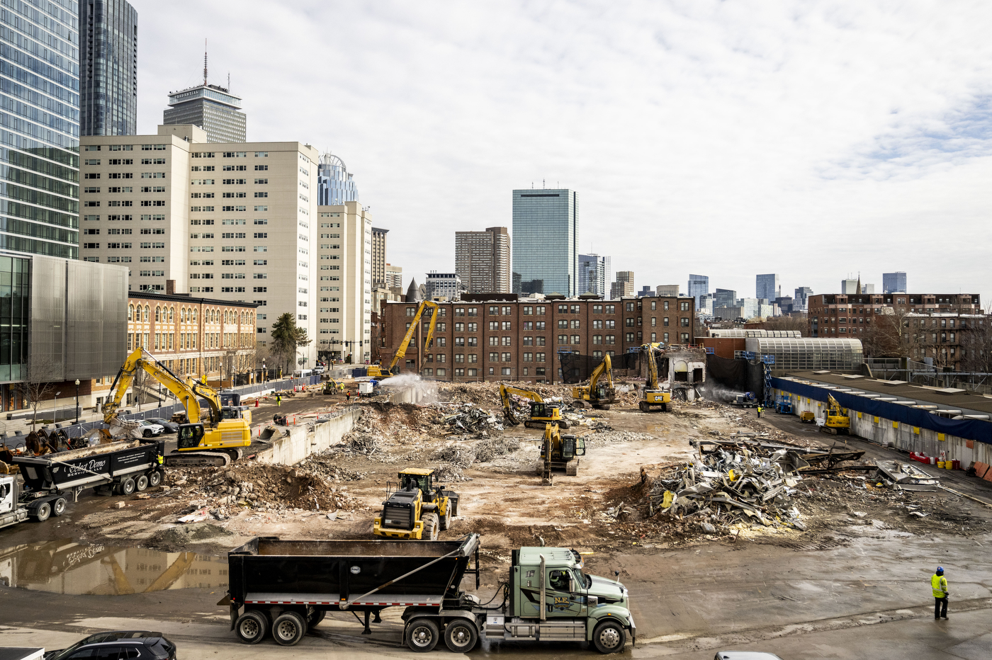 A wide view of the construction site showing multiple vehicles taking down the final pieces of the former Matthews Arena.