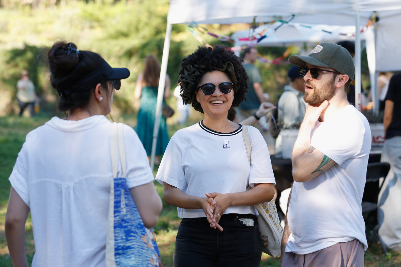 Three people wearing white shirts stand outside and chat with each other next to a white tent. 