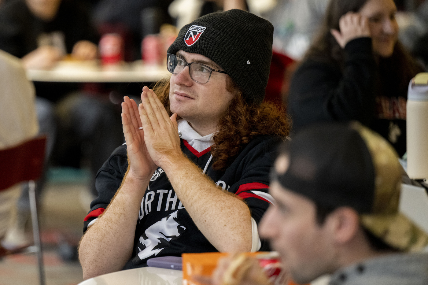 Student clasps hands while watching Northeastern vs. Ohio State at a Curry Student Center watch party.