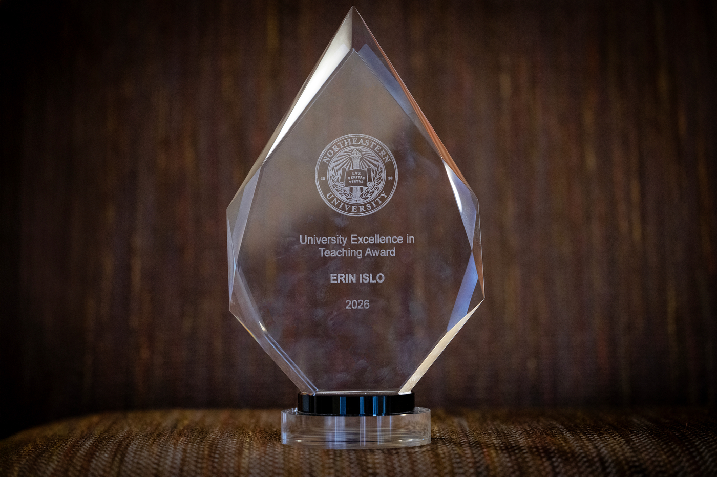 The see through, diamond-shaped University Excellence in Teaching Award stands on a table, with Erin Islo's name engraved in it.