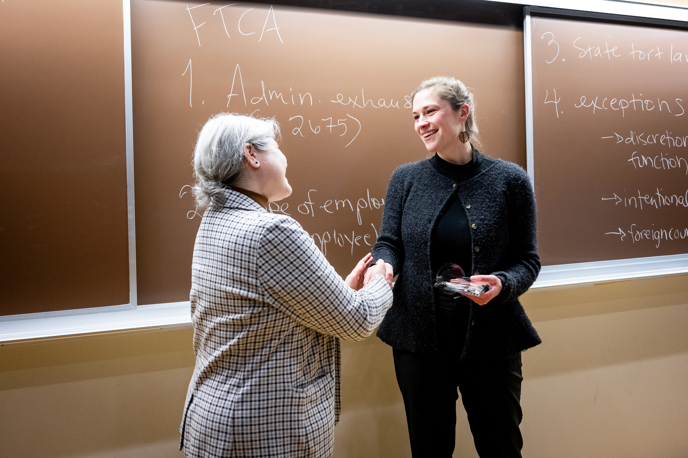 Erin Islo shakes hands with Provost Beth Winkelstein while holding her University Excellence in Teaching Award.