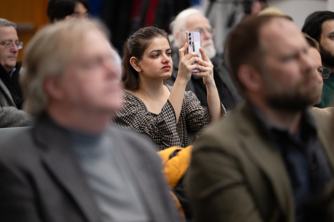 Audience members listening to Koen Pauwels lecture with one person in the middle ground holding up their phone to record or photograph the event. 