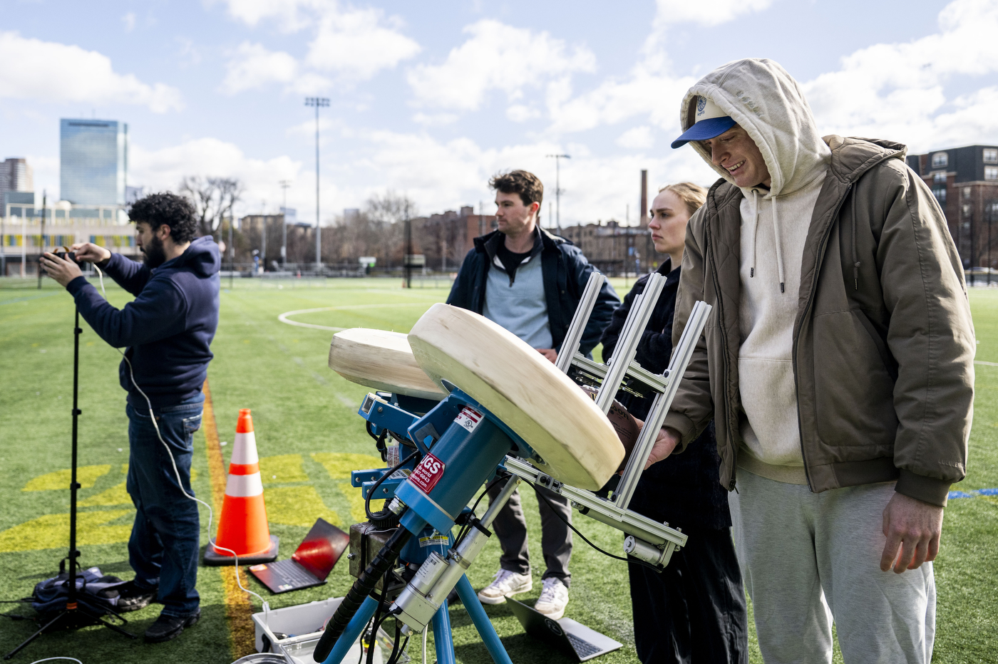Four students set up an autonomous football-launching machine outside on a turf field. 
